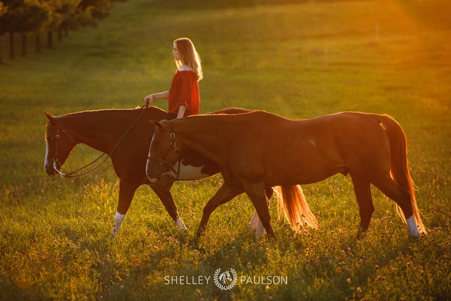 Photo of a girl riding her horse while leading another.